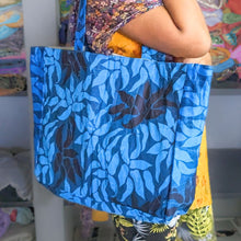 Load image into Gallery viewer, A large tote bag made from upcycled sari fabric, held by a person with a colorful garment in the background. The bag features a geometric pattern in shades of blue.