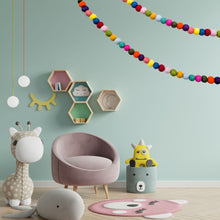 Load image into Gallery viewer, Children's room with a pink chair, colourful felt garland decor, and toys on a light green wall.