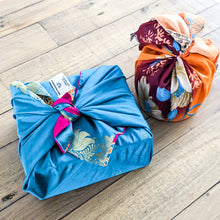 Load image into Gallery viewer, Two wrapped packages on a wooden surface, one blue with gold patterns and the other multicolored.