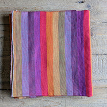 Load image into Gallery viewer, A folded fabric scarf featuring vertical stripes in a rainbow of colours including pink, purple, orange, red, green, and beige, displayed on a rustic wooden background
