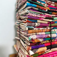 Load image into Gallery viewer, Stack of sari patchwork cushion covers piled on a wooden surface against a white wall
