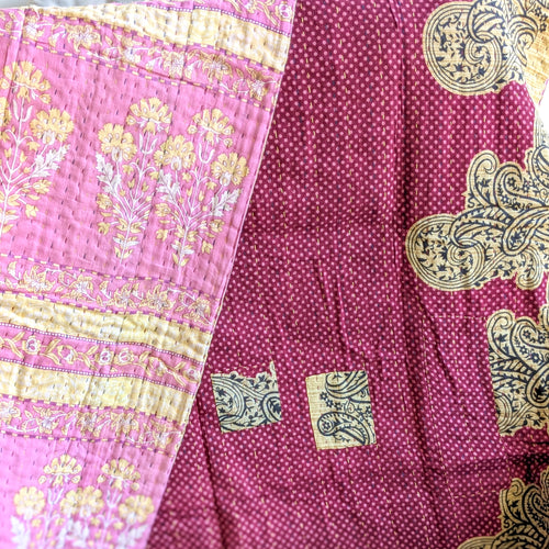 Close-up of a pink and beige patterned fabric kantha quilt with intricate designs.