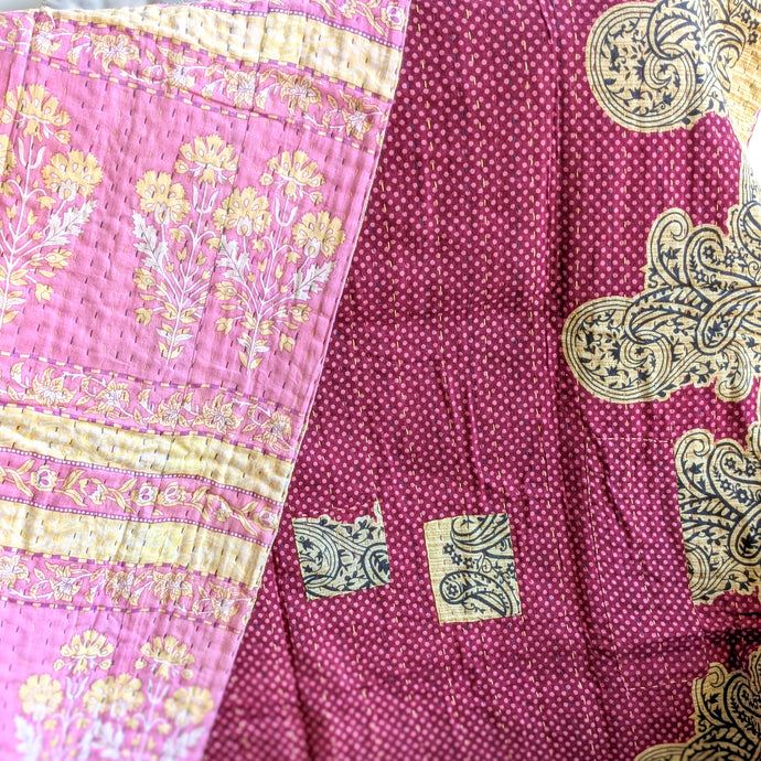 Close-up of a pink and beige patterned fabric kantha quilt with intricate designs.