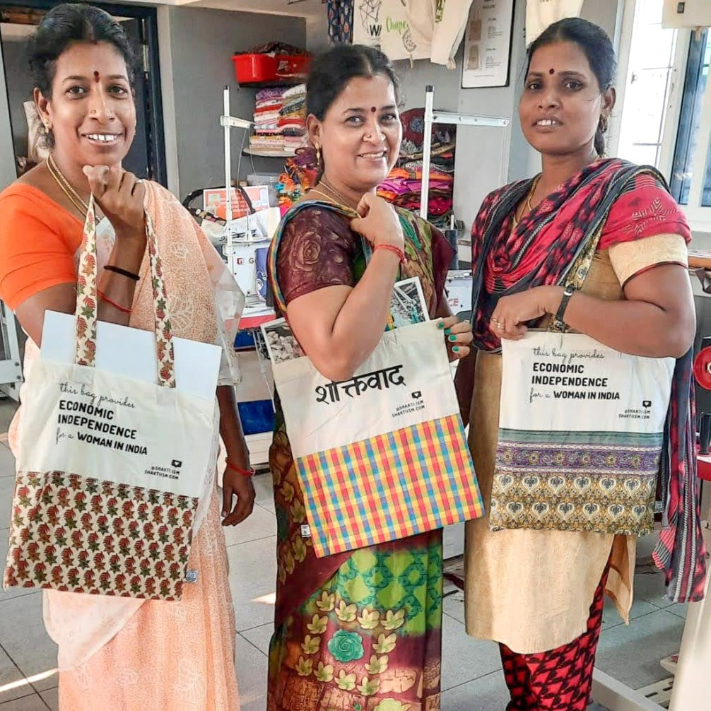 3 artisans smiling and holding sari tote bags